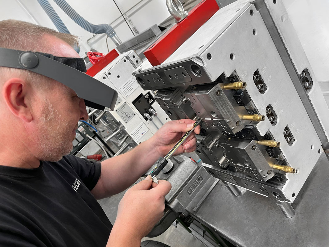 ein Mitarbeiteter der Firma Schnitzer Kunststoffe arbeitet mir der Lupenbrille sehr präzise an einem Spritzguss Werkstück