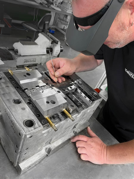 ein Mitarbeiteter der Firma Schnitzer Kunststoffe arbeitet mir der Lupenbrille sehr präzise an einem Spritzguss Werkstück