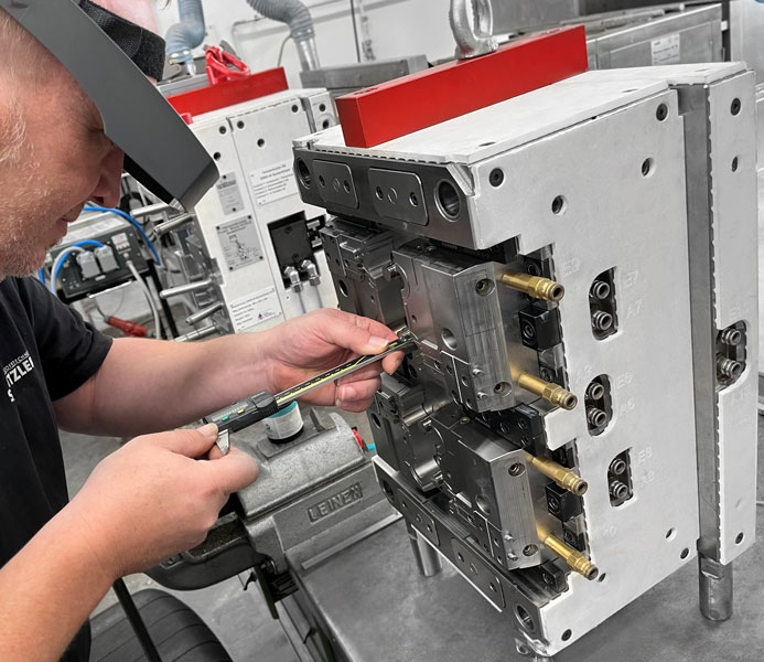 ein Mitarbeiteter der Firma Schnitzer Kunststoffe arbeitet mir der Lupenbrille sehr präzise an einem Spritzguss Werkstück