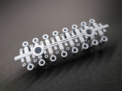 graues Mehrfach-Kavitäten-Spritzgussteil für die Primärverpackung von Zahnfüllmaterial, ausgestattet mit dem Schnitzler-Logo. Das Teil wird mit einem 32-fach Werkzeug und vier Nadelverschlussdüsen inline produziert. Es wurde 100% auf Kanülendurchfluss und Kanülenlänge geprüft und anschließend verpackt.